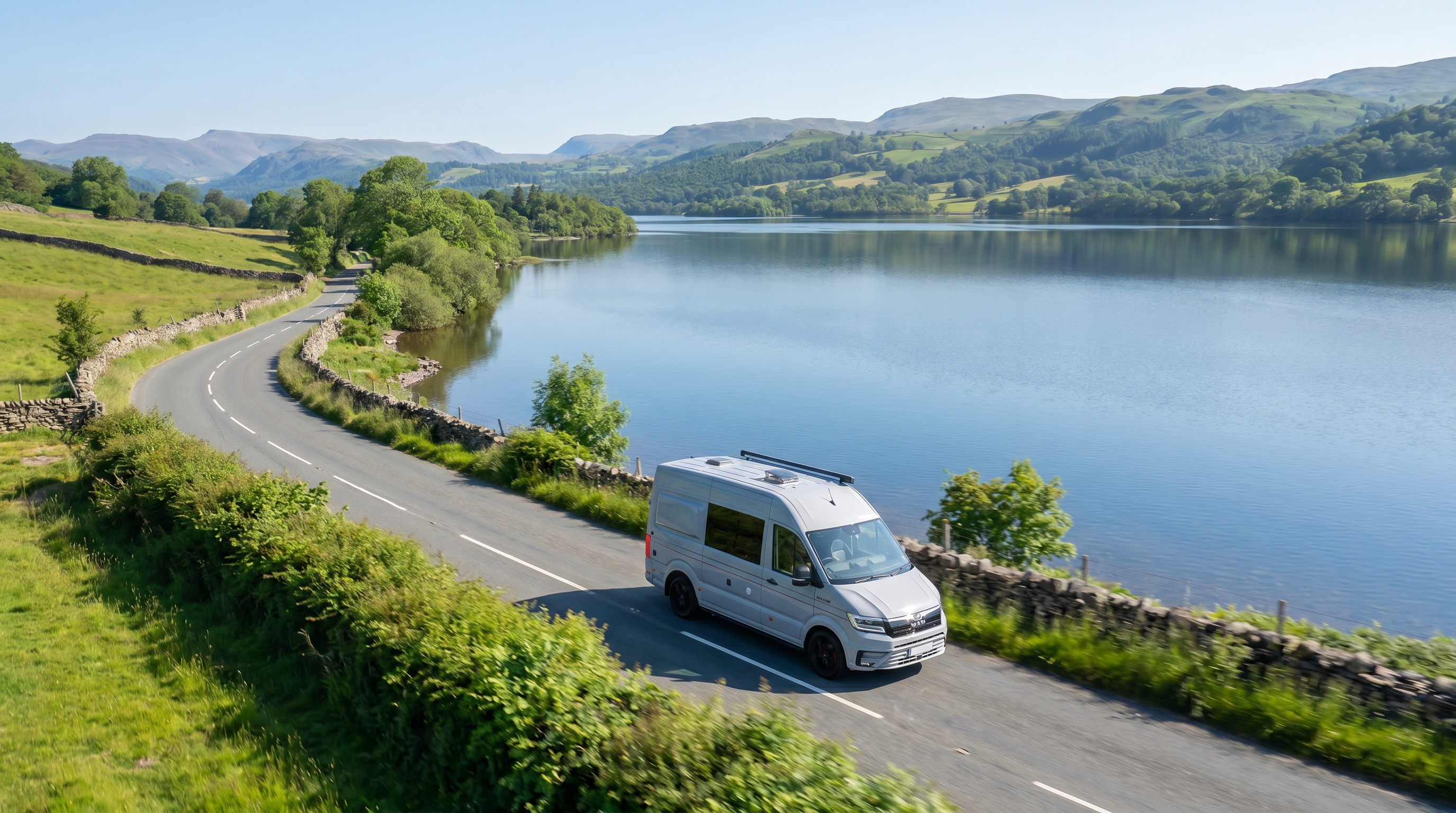 White van on a scenic road by a lake with mountains in the background