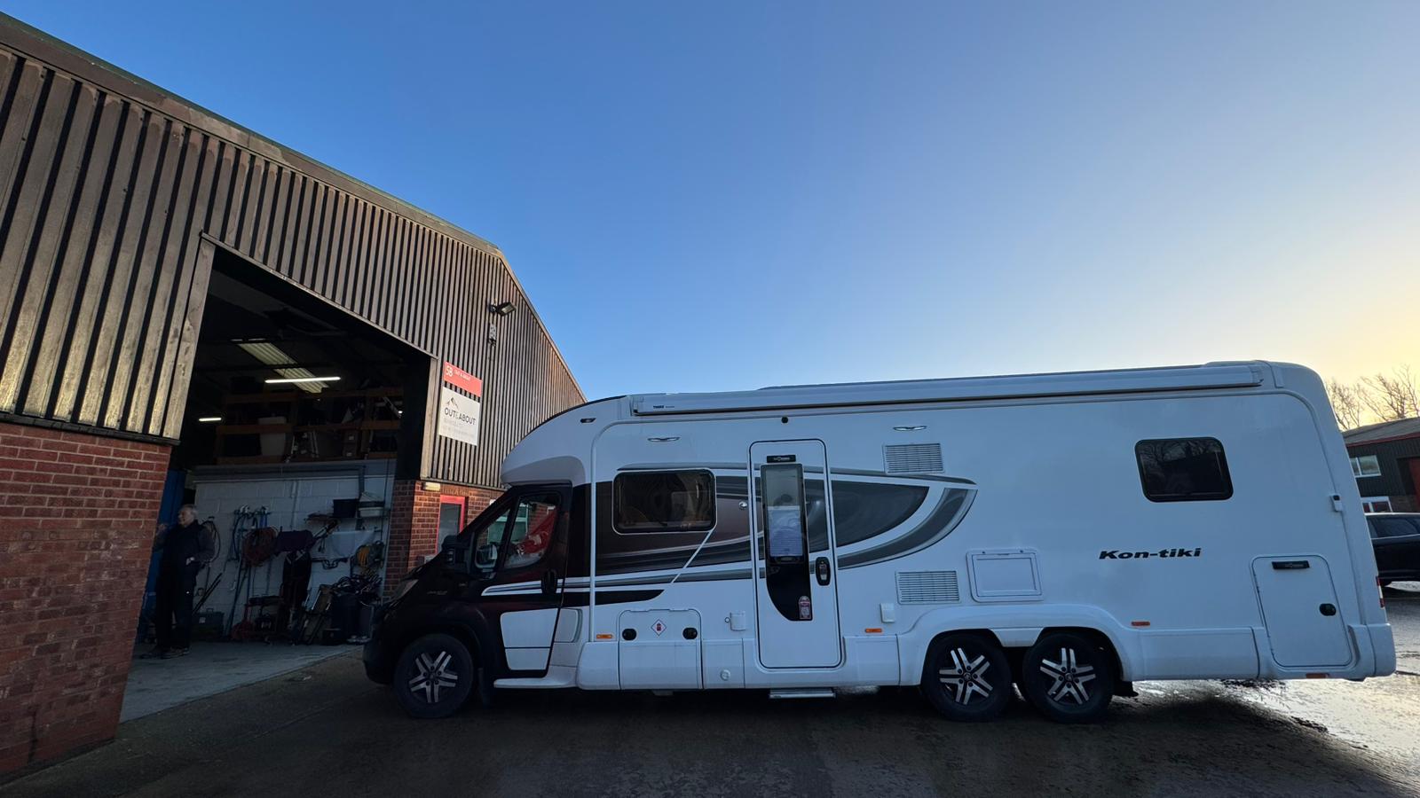 White RV parked outside a building with a clear blue sky.